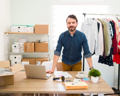 Hispanic young entrepreneur behind his office desk and working on making packages with fashion clothes to ship to their customers